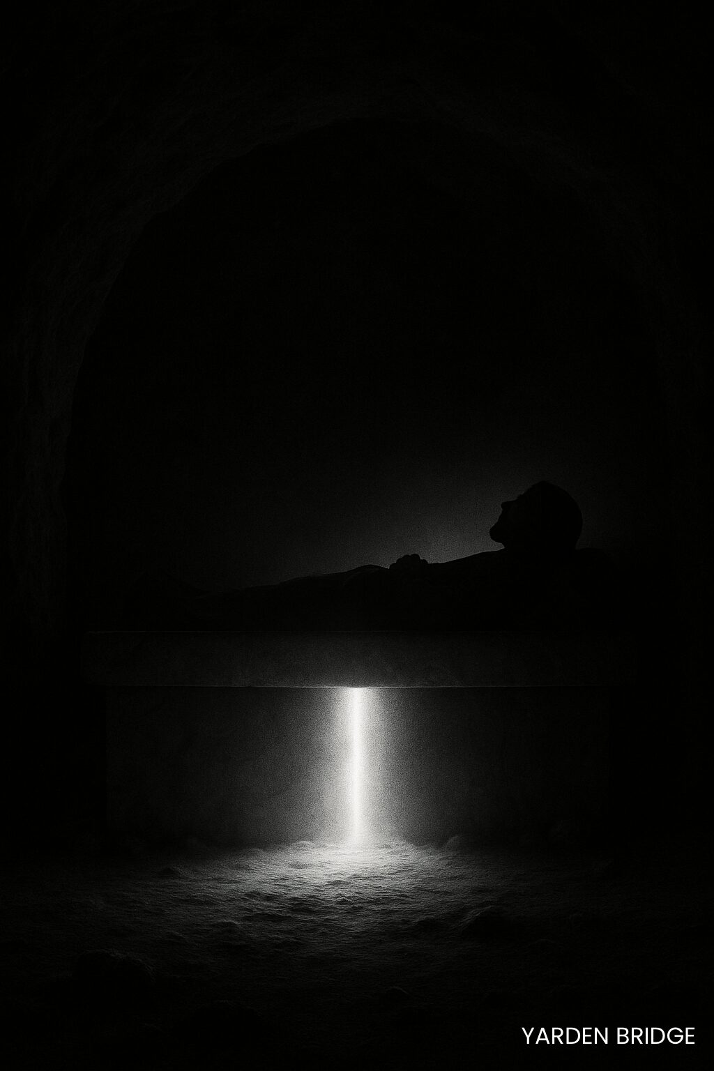 The Reverser. High-contrast black-and-white photograph of a stone slab in a cave, with a man’s figure lying upon it as light breaks through the darkness, symbolizing Christ the Reverser who makes His bed in the grave and overturns death.